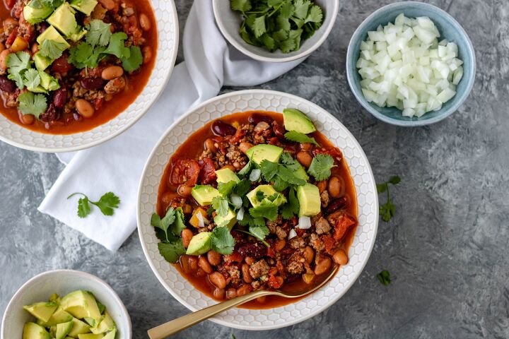 30 minute chicken chipotle chili, Two bowls of Chicken Chipotle Chili topped with avocado chunks diced onion and fresh cilantro