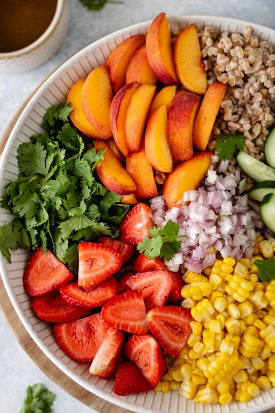 peach cilantro farro salad, A large serving bowl of ingredients like sliced peaches strawberries corn red onion and cilantro alongside a pinch bowl of homemade vinaigrette