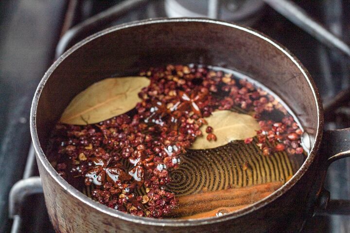 homemade spicy chili oil, simmering oil spices peppercorns in a pot over a black stove