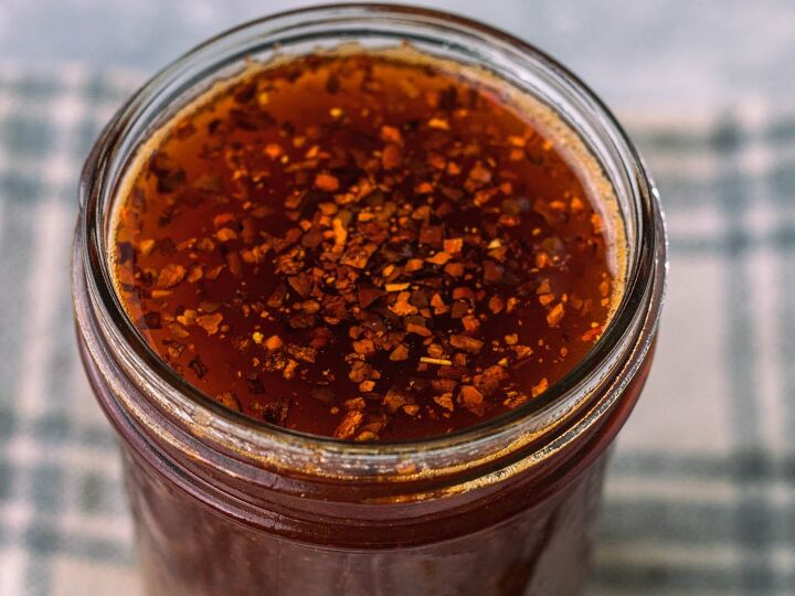 homemade spicy chili oil, red oil with red flecks floating on top in a jar with a light gray background behind