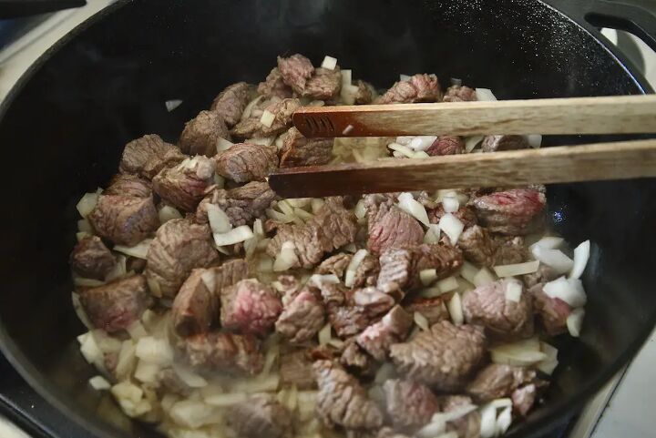 easy hungarian beef goulash recipe, chunks of meat in cast iron dutch oven with onion pieces