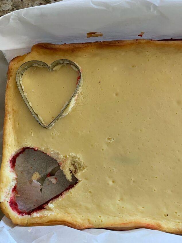 Cooked pan of cheesecake being cut by heart shaped cookie cutter