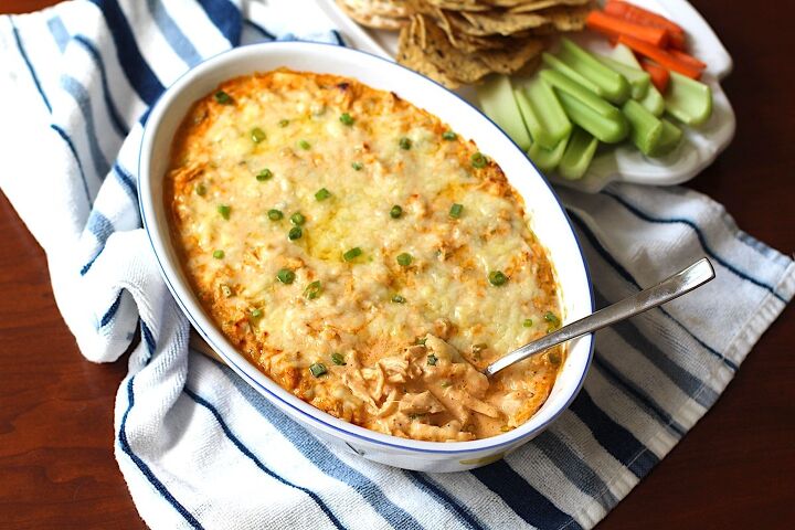 buffalo chicken dip with greek yogurt, Buffalo Chicken Dip with greek yogurt in serving dish with spoon in it On the side is a plate of celery carrots and chips