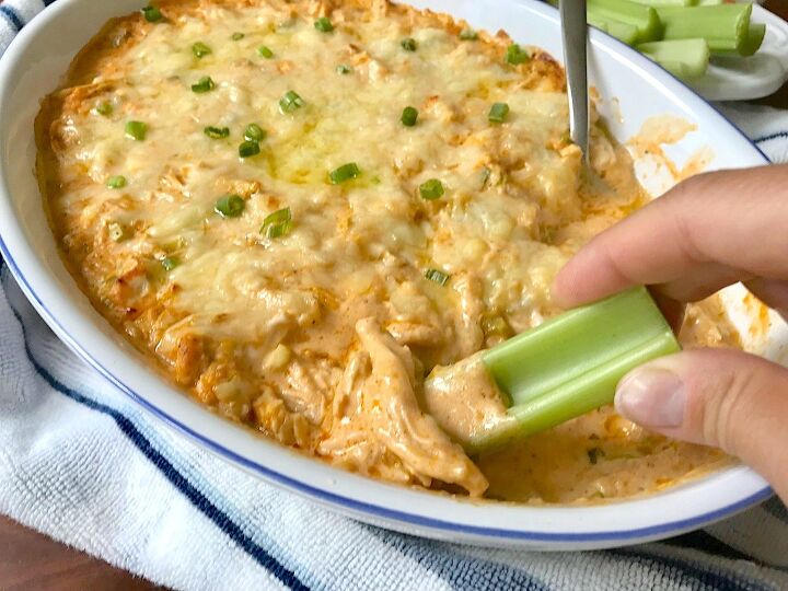 buffalo chicken dip with greek yogurt, Hand with celery scooping Buffalo Chicken Dip with greek yogurt in serving dish with spoon in it