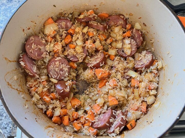 galinhada dutch oven chicken and rice, Uncooked rice mixed into sausage carrots onions and garlic cooking in a pot for Galinhada Dutch Oven Chicken and Rice