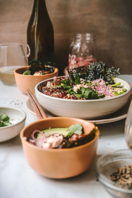 poke bowl with spicy mayo, A Pok bowl on a table with smaller bowls around it glasses of wine and a jar of pickled onions