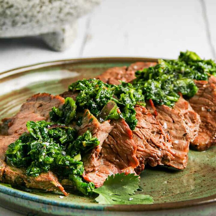 flank steak with chimichurri, Flank Steak with Chimichurri Photographed on a green plate on top of a white wood background