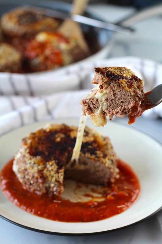 polpettone cheese stuffed meatballs, A Ground beef Polpettone sitting on tomato sauce on a plate with a fork pulling a piece up with a long mozzarella cheese pull