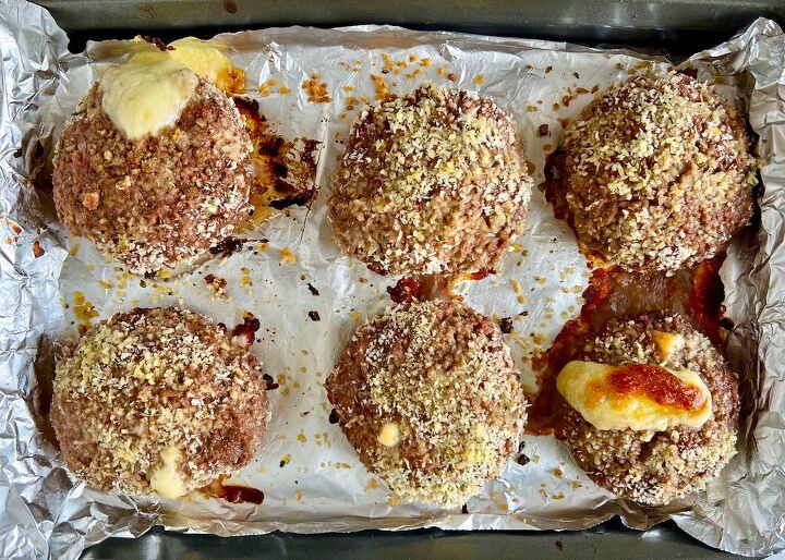 polpettone cheese stuffed meatballs, Six cooked breaded polpettone beef patties on an aluminum lined sheet pan with cheese oozing out of two patties