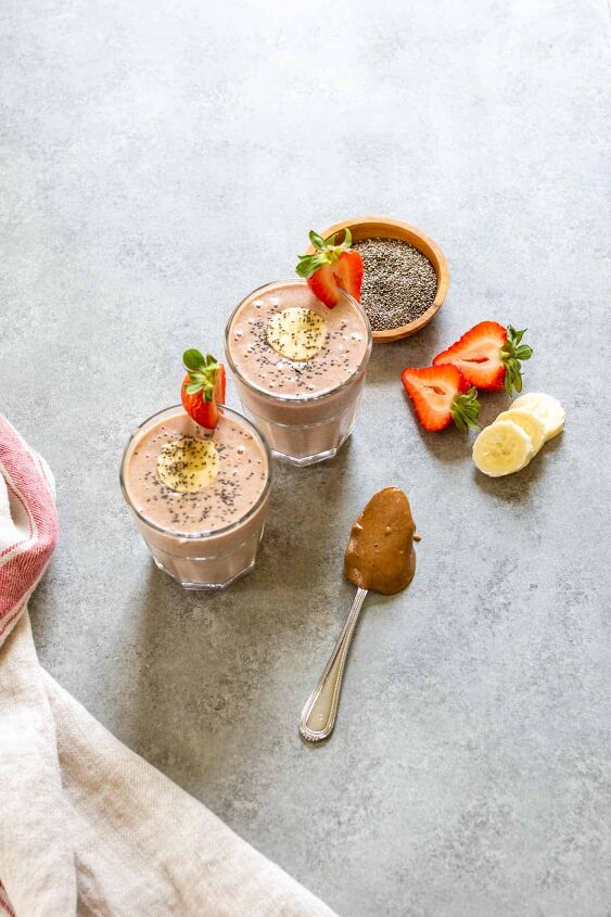 strawberry banana peanut butter smoothie, two strawberry banana peanut butter smoothies in glasses with fruit and peanut butter on the side