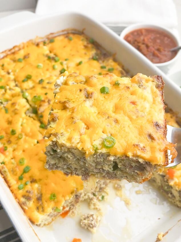 easy cheesy sausage egg bake, spatula with one slice of egg bake with casserole dish of egg bake in background