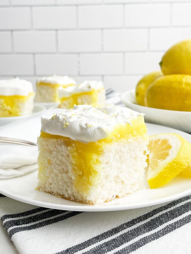 lemon poke cake, piece of lemon poke cake on white plate with bowl of lemons and plates of cake in background