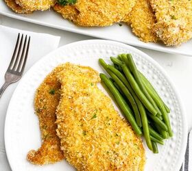 crispy baked thin chicken breasts, white plate with two baked thin chicken breasts and green beans with platter of chicken in background