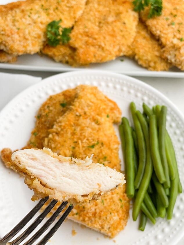 crispy baked thin chicken breasts, fork holidng up a bite of panko chicken with plate of chicken in background