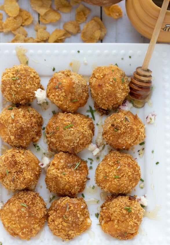 air fryer goat cheese sweet potato bites, A square white dish with air fried goat cheese and sweet potato balls They re drizzled with honey you can see the honey stick with honey oozing off of it The dish is sprinkled with fresh rosemary and there s corn flakes in the background