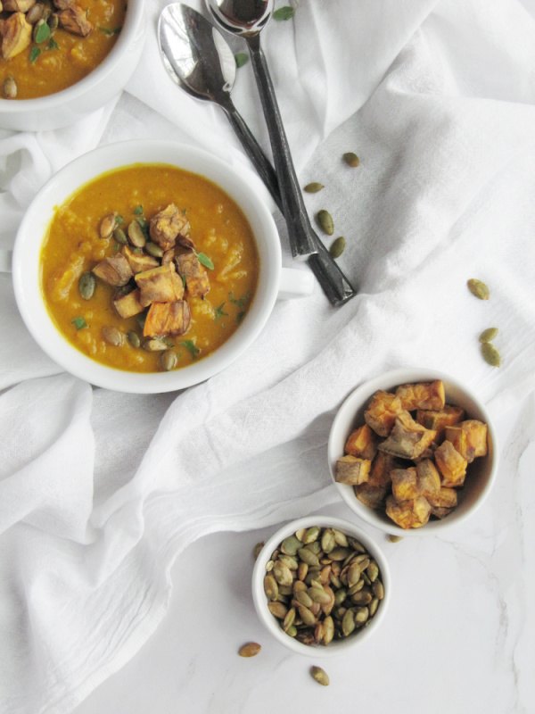 sweet potato and pumpkin soup, Soup in white bowls with 2 spoons and two small bowls of potatoes and pumpkin seeds