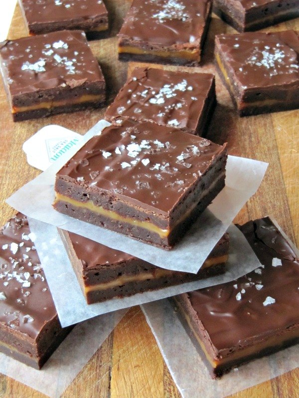 fudgy caramel stuffed brownies with sea salt, chocolate brownies with a layer of caramel sprinkled with sea salt layered on parchment paper on a cutting board