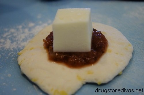 A dollop of marinara sauce and a square of cheese in a flattened piece of biscuit