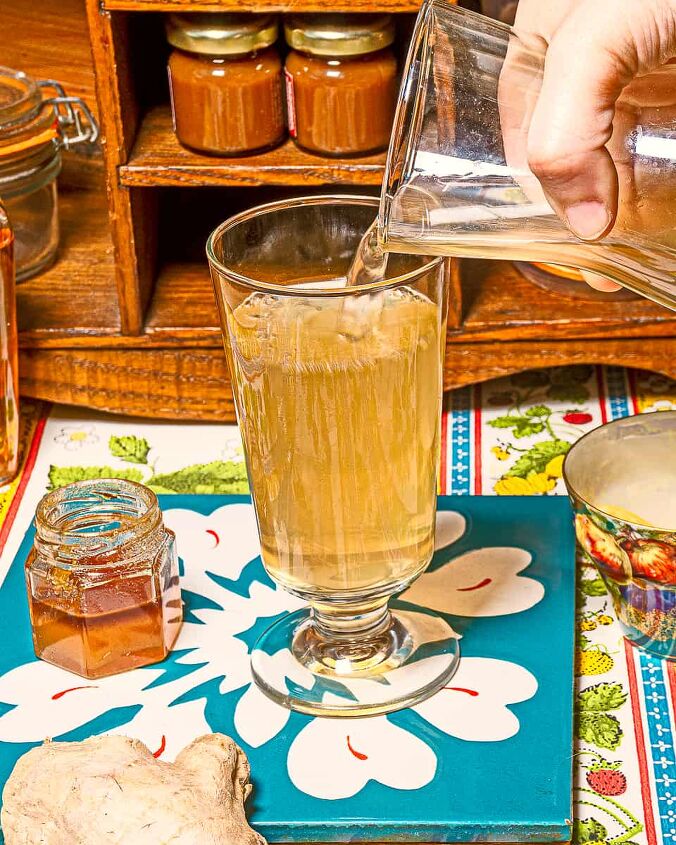 ginger water, Person pouring ginger infused water into a tall glass with a small jar of honey to the left of it