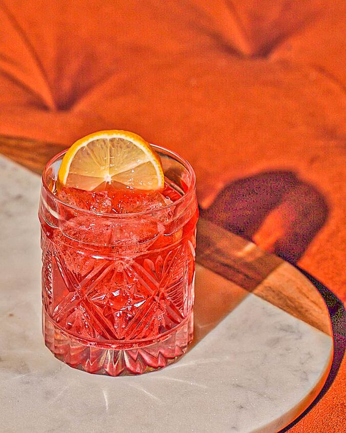 negroni sbagliato, Red liquid in a cut glass with a lemon wheel garnish on a marble tray on an orange couch
