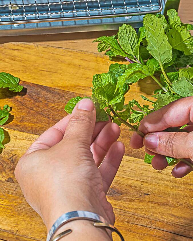 how to make herbed salt, person pulling a mint leaf off of asprig of mind with a pile of mild sprigs on a wooden cutting board