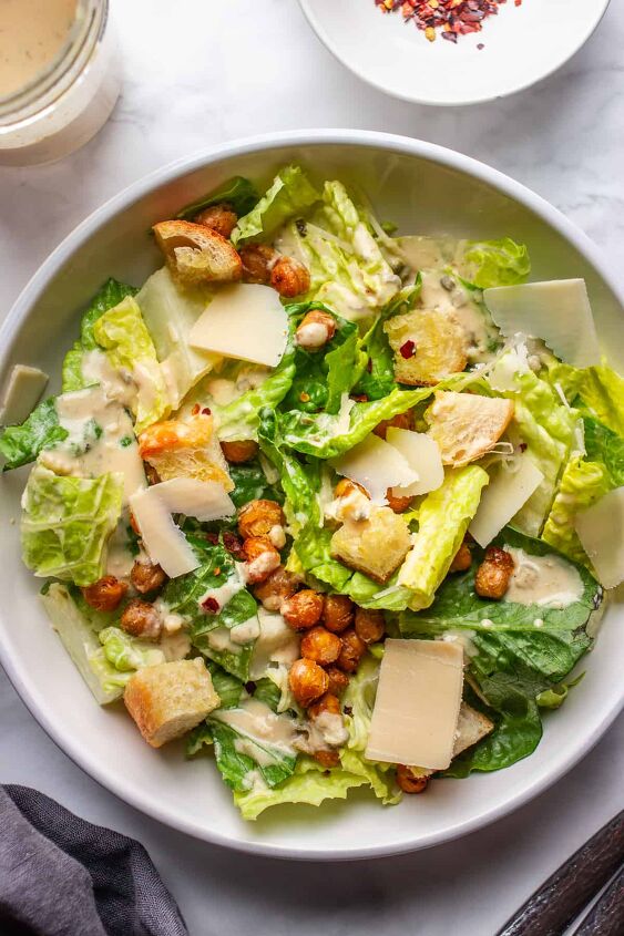 crowd pleasing vegan caesar salad you won t believe it s dairy free, A bowl of the best dairy free Caesar salad next to a small bowl with red pepper flakes and Tahini dressing
