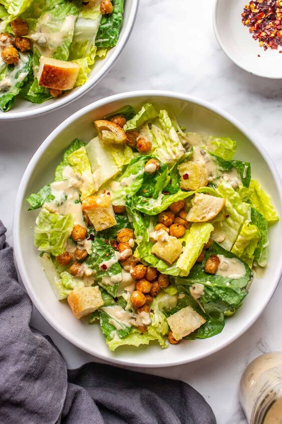 crowd pleasing vegan caesar salad you won t believe it s dairy free, Two bowls of creamy dairy free Caesar s salad on a white table with a grey napkin on a side