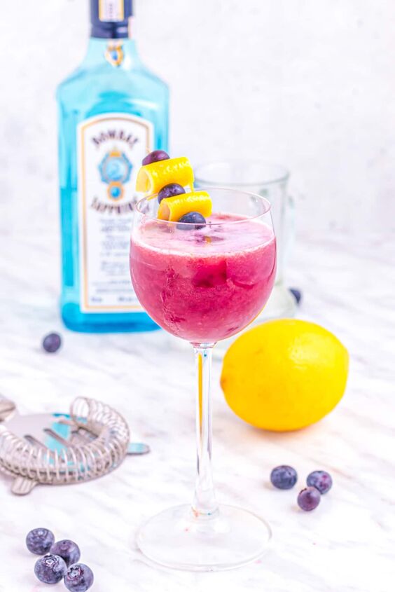 blueberry gin sour cocktail, blueberry gin sour on table with lemon and blueberries