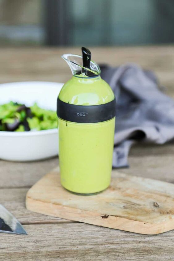 keto vegan avocado dressing recipe gluten free, bottle of vegan avocado dressing recipe in a salad dressing container on a cutting board with a knife