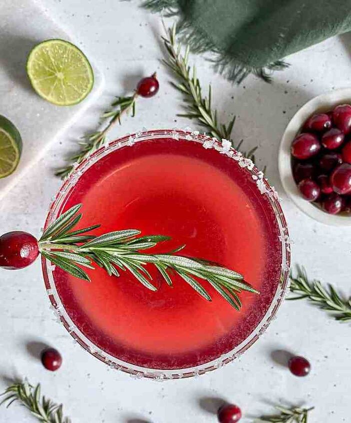 A red cocktail in a glass with a salted rim A garnish of rosemary and a cranberry are on top of the drink