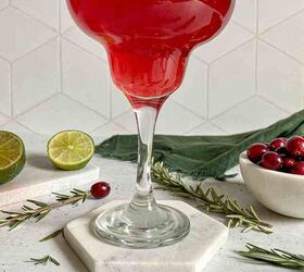 A red margarita in a glass with a salt rim surrounded by fresh cranberries and limes