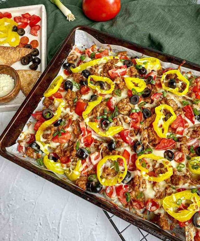 italian nachos happy honey kitchen, Italian Nachos on a sheet pan topped with sausage alfredo sauce cheese tomatoes olives and peppers A tray with extra toppings green onions and grated cheese is next to the pan