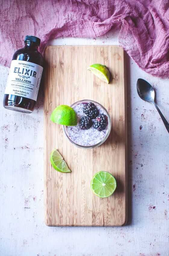 blackberry lime chia seed wellness parfait, top view shot of a cutting board with a glass of chia parfit sitting on it garnished with lime wedges and blackberries