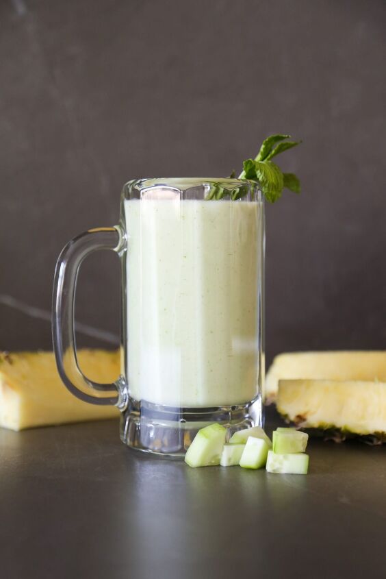 pineapple cucumber smoothie detoxifying and delicious, pineapple cucumber smoothie in a glass with chopped cucumber chunks and wedges of pineapple garnish
