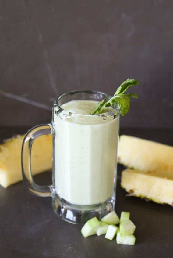 pineapple cucumber smoothie detoxifying and delicious, pineapple cucumber smoothie in a glass with chopped cucumber chunks and wedges of pineapple garnish