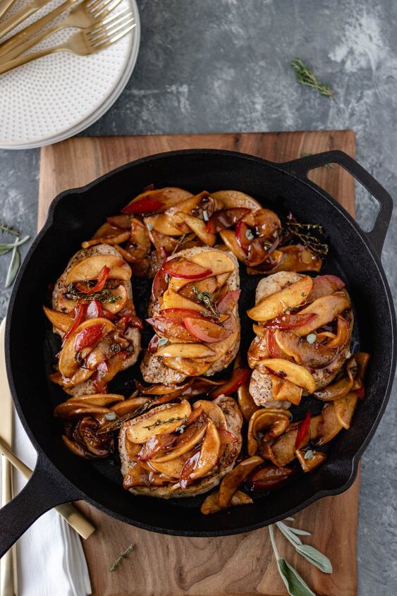 apple plum pork chops with herbs, Cooked pork chops in a skillet topped with cooked apple and plums slices and sitting on a wood cutting board