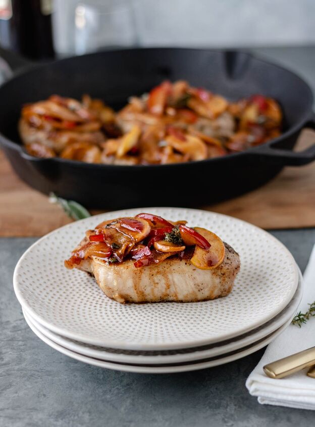 apple plum pork chops with herbs, A cooked pork chop with apple and plum slices sitting on a stack of plates