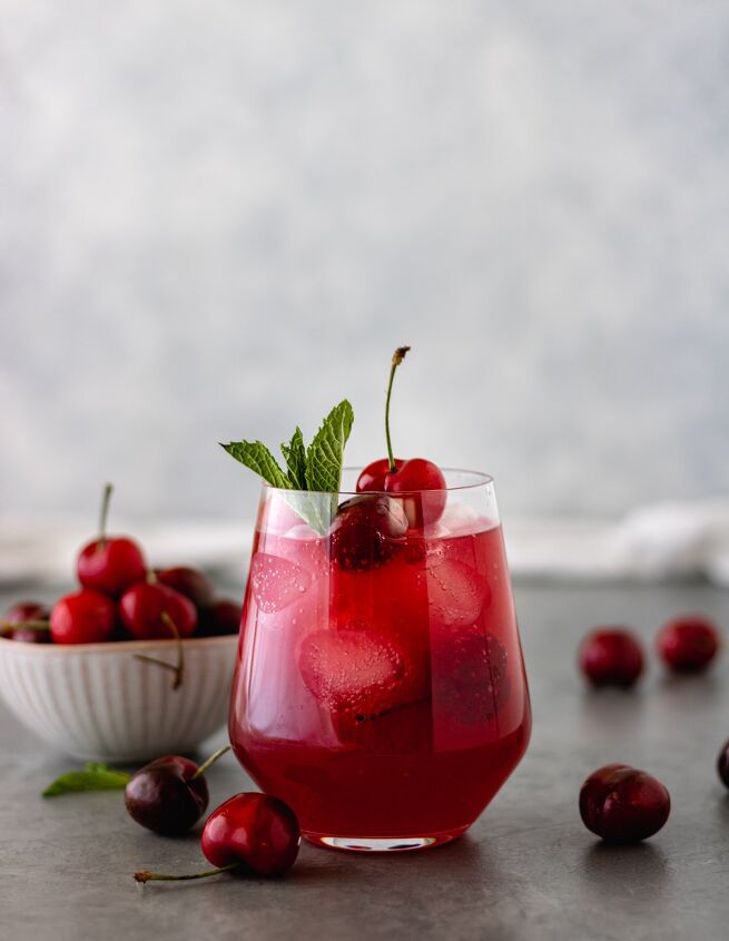 cherry berry gin kombucha cocktail, A glass of a Cherry Berry Gin Kombucha Cocktail topped with fresh cherries and mint and surrounded by fresh cherries