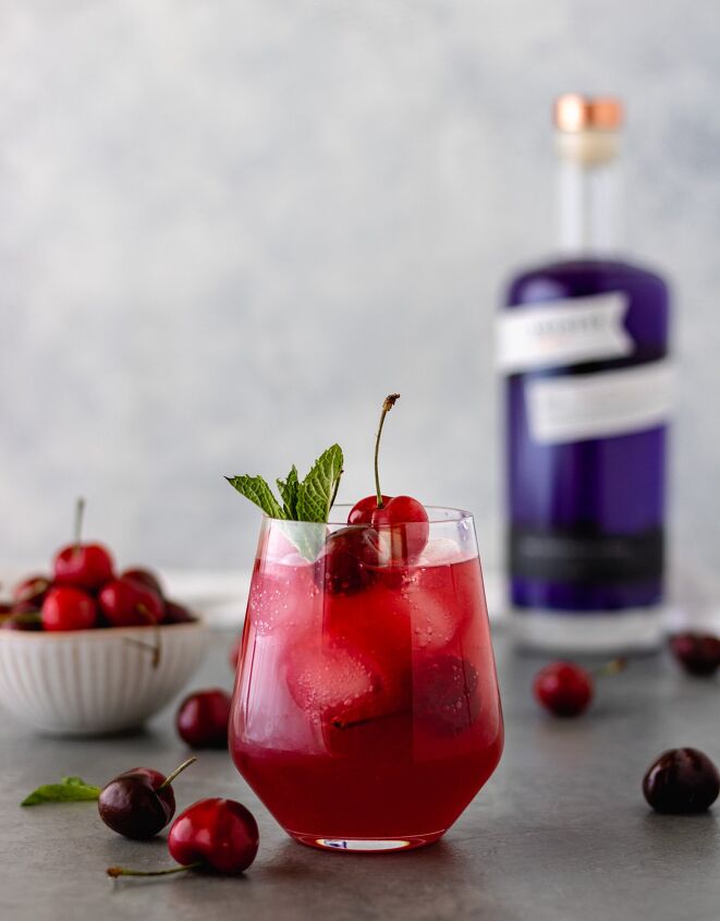 cherry berry gin kombucha cocktail, A glass of a Cherry Berry Gin Kombucha Cocktail surrounded by fresh cherries and a bottle of Empress 1908 Gin