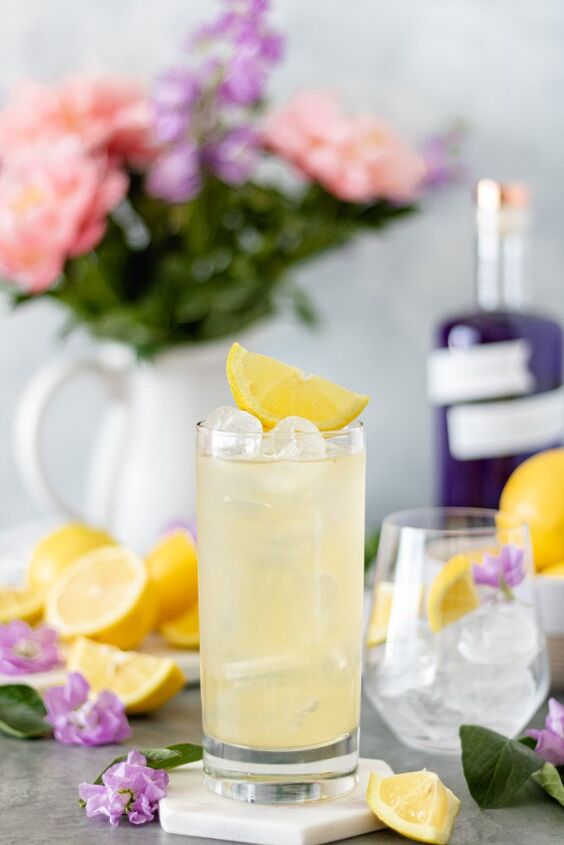 honey lavender gin lemonade with empress, A glass of fresh Lemonade sitting on a marble trivet and topped with a fresh lemon slice