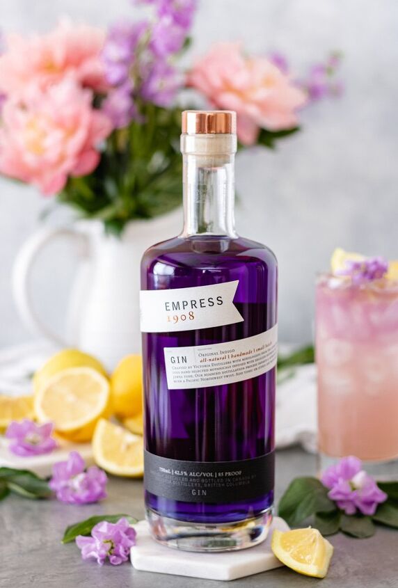 honey lavender gin lemonade with empress, A bottle of Empress 1908 Gin surrounded by a glass of Empress Gin Lemonade fresh lemons and flowers