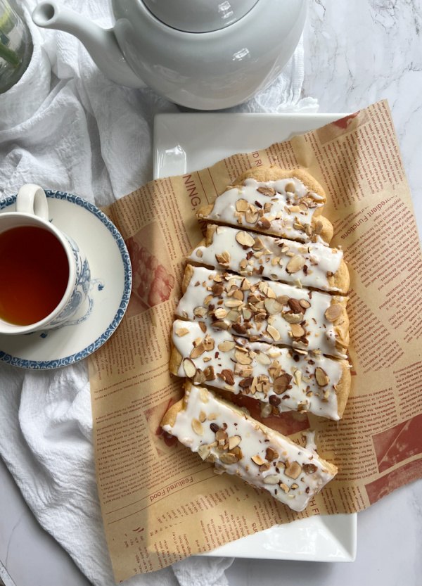 almond kringle, almond kringle danish puff pastry on a white platter with a cup of tea
