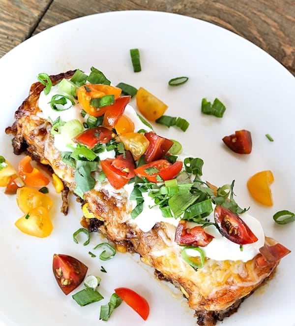 beef enchilada casserole recipe 5ingredient simple, enchilada casserole on a white plate sitting on a wooden table