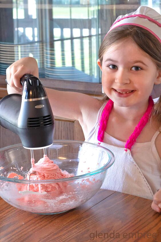 6 year old girl mixing strawberry cake mix cookie dough with an electric hand mixer in a clear glass bowl