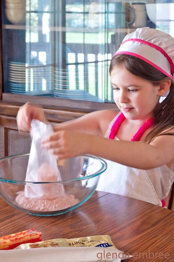 6 year old girl emptying cake mix into a clear glass bowl for strawberry cake mix cookies