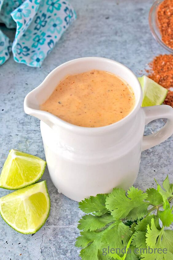 cashew queso easy 3ingredient vegan dip, Southwest Dressing in White Pitcher on concrete counter with limes cilantro spices and blue print fabric