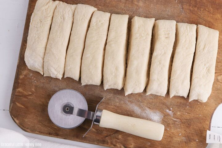 copycat olive garden bread machine breadsticks, Bread dough cut into strips sitting on a wooden cutting board with a pizza cutter next to it