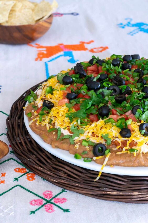 Mexican Layer Dip on a brown rattan platter on an embroidered tablecloth