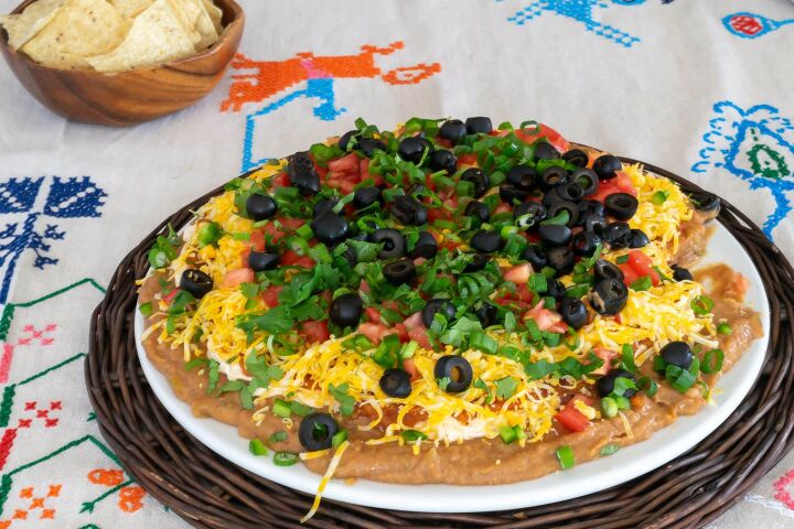 Layered Taco Dip on a brown rattan platter on an embroidered tablecloth