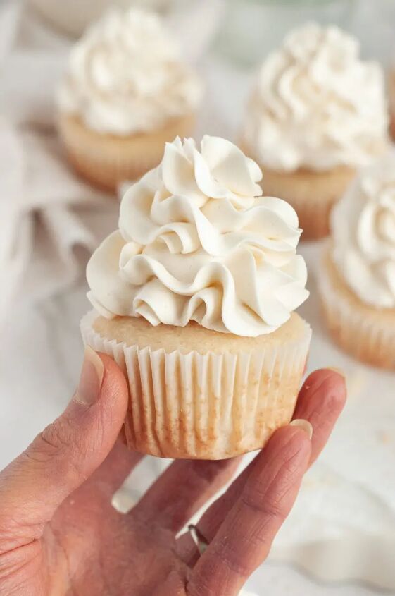 gluten free vanilla cupcakes dairy free, A hand is holding a vanilla cupcake that is topped with white fluffy buttercream frosting